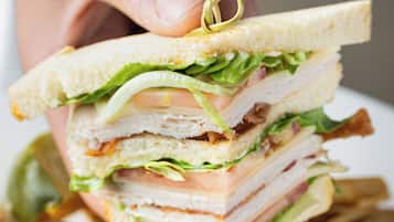 Un sándwich con varias capas de ingredientes, sostenido por una mano, con una porción de papas fritas al fondo.