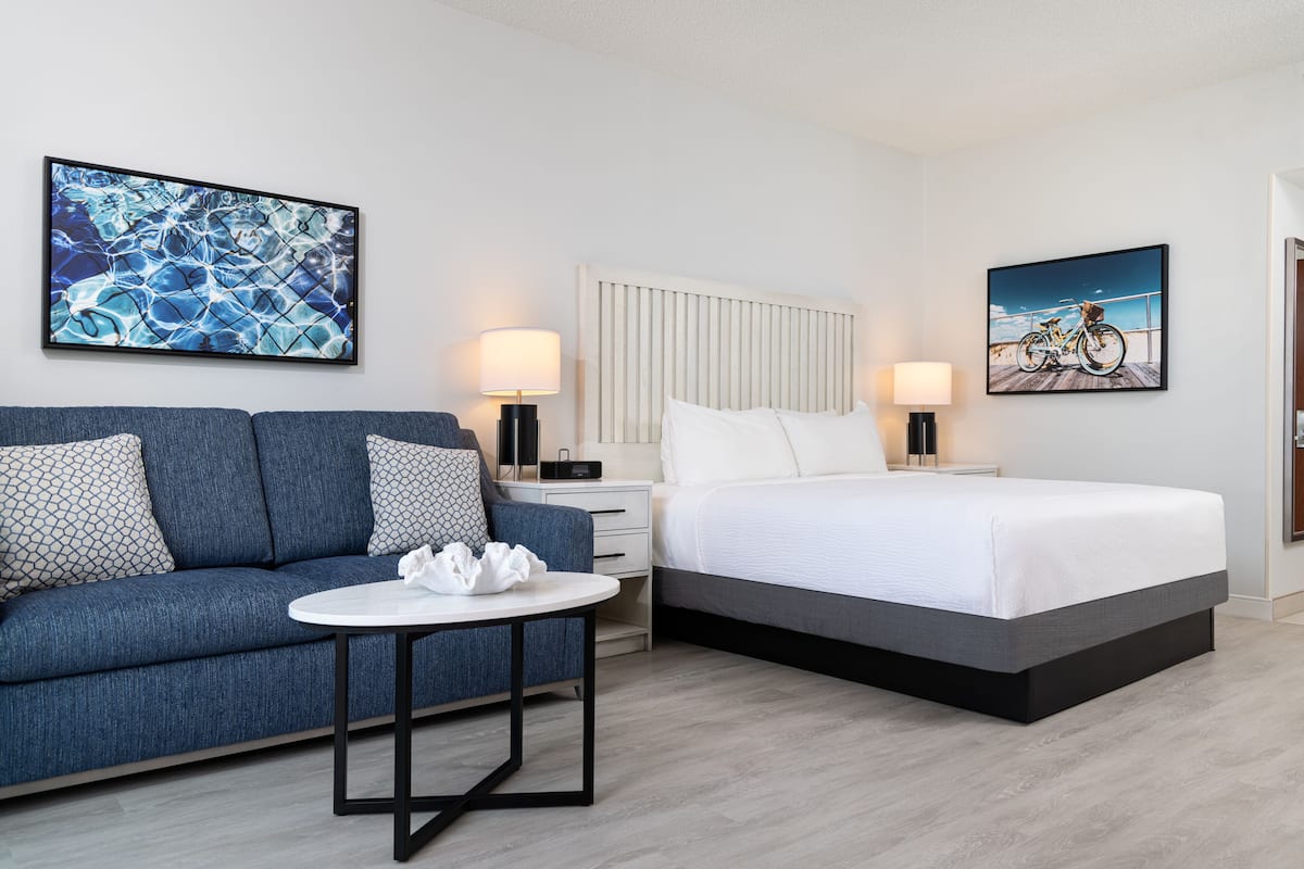 A modern hotel room with a bed, a sofa, a small table, and two wall-mounted lamps.