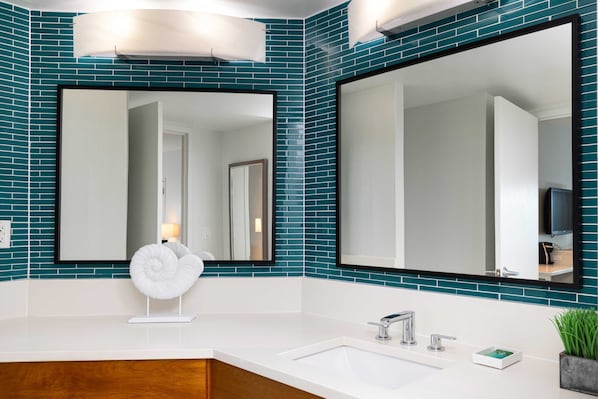 Un baño moderno con mosaicos azules, un lavamanos blanco y dos espejos grandes.
