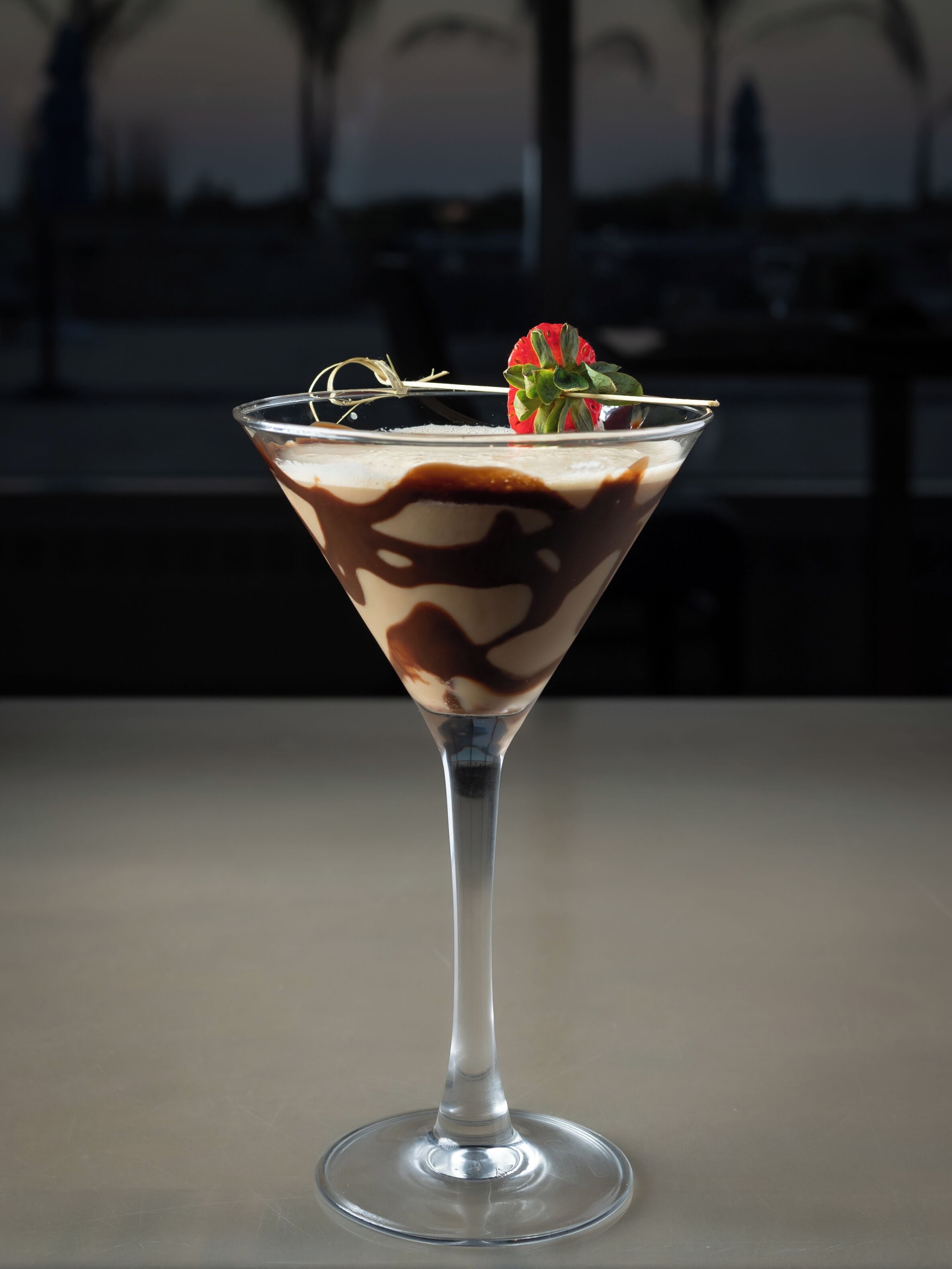 A martini glass with a layered drink, garnished with a strawberry, on a table.