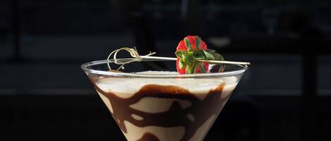 A martini glass with a layered drink, garnished with a strawberry, on a table.