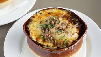 Un plato de papas al horno cubiertas de queso y cebollas, servido en un recipiente de cerámica marrón sobre un plato blanco.