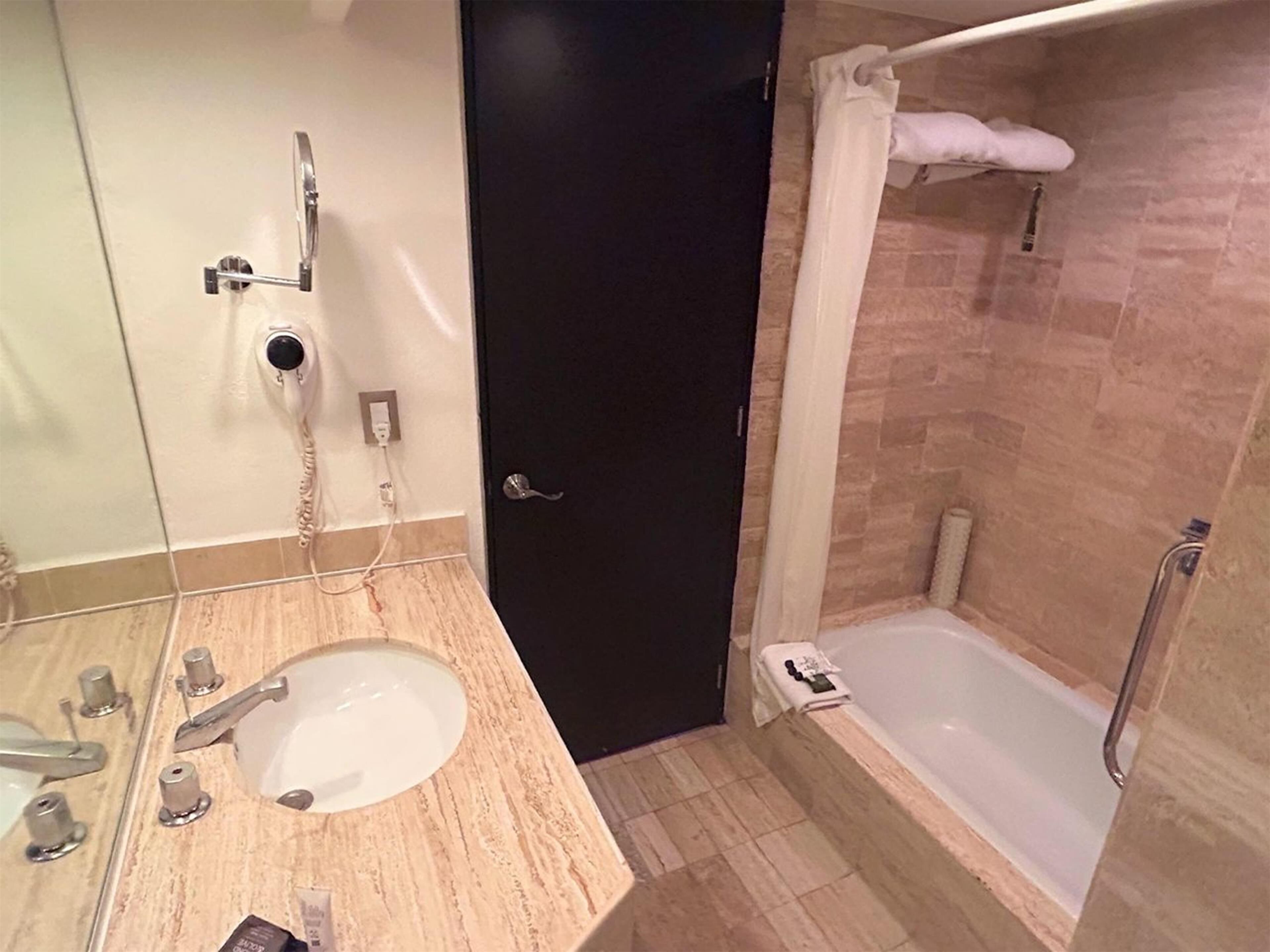 Un baño con lavamanos, espejo, toallero, ducha y puerta.