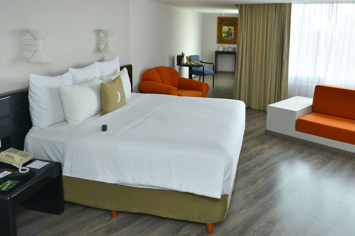 A hotel room with a large bed, an orange sofa, a desk with a phone, and a painting on the wall.