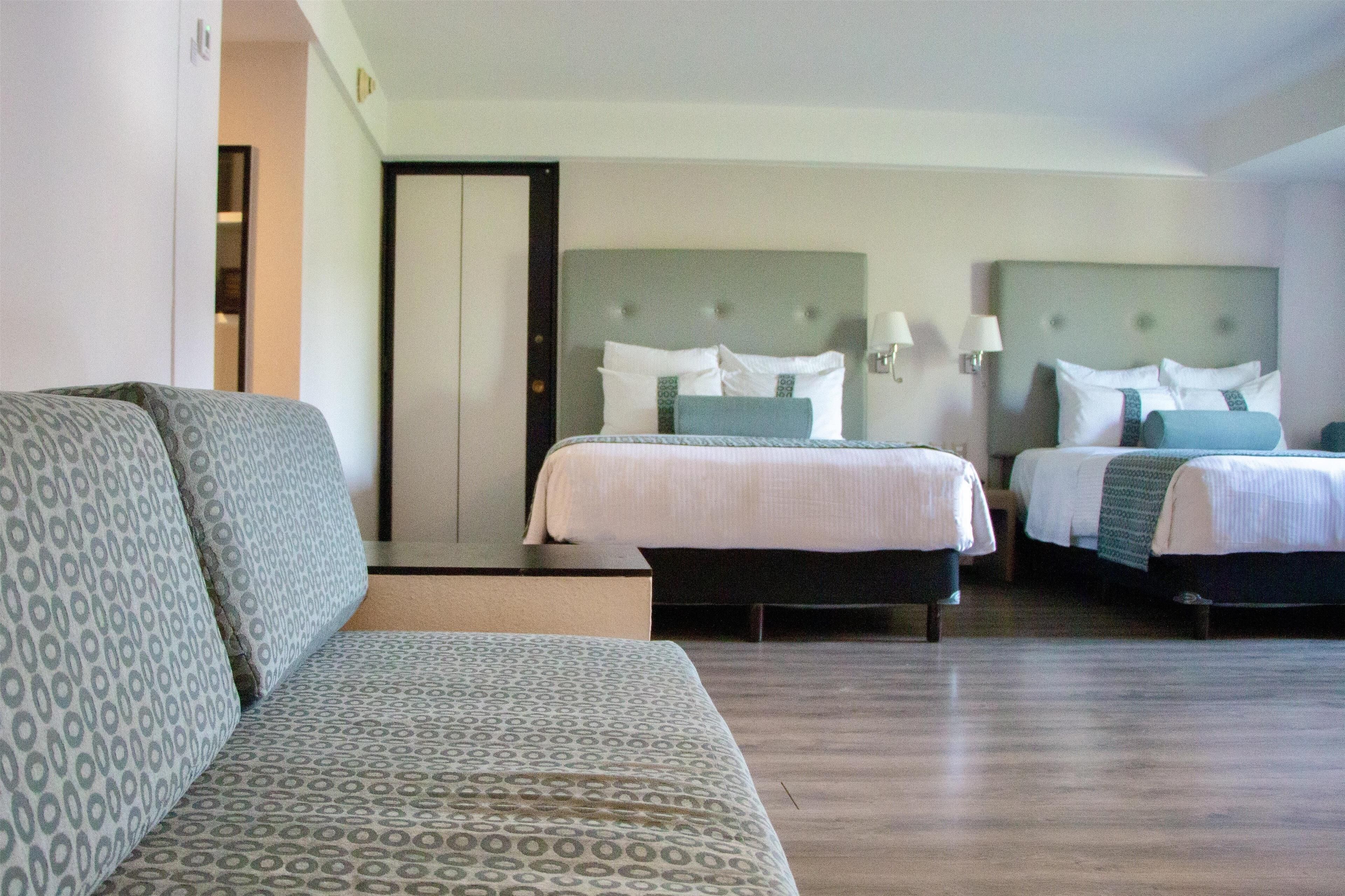 A hotel room with two beds, a sofa, and a mirror.
