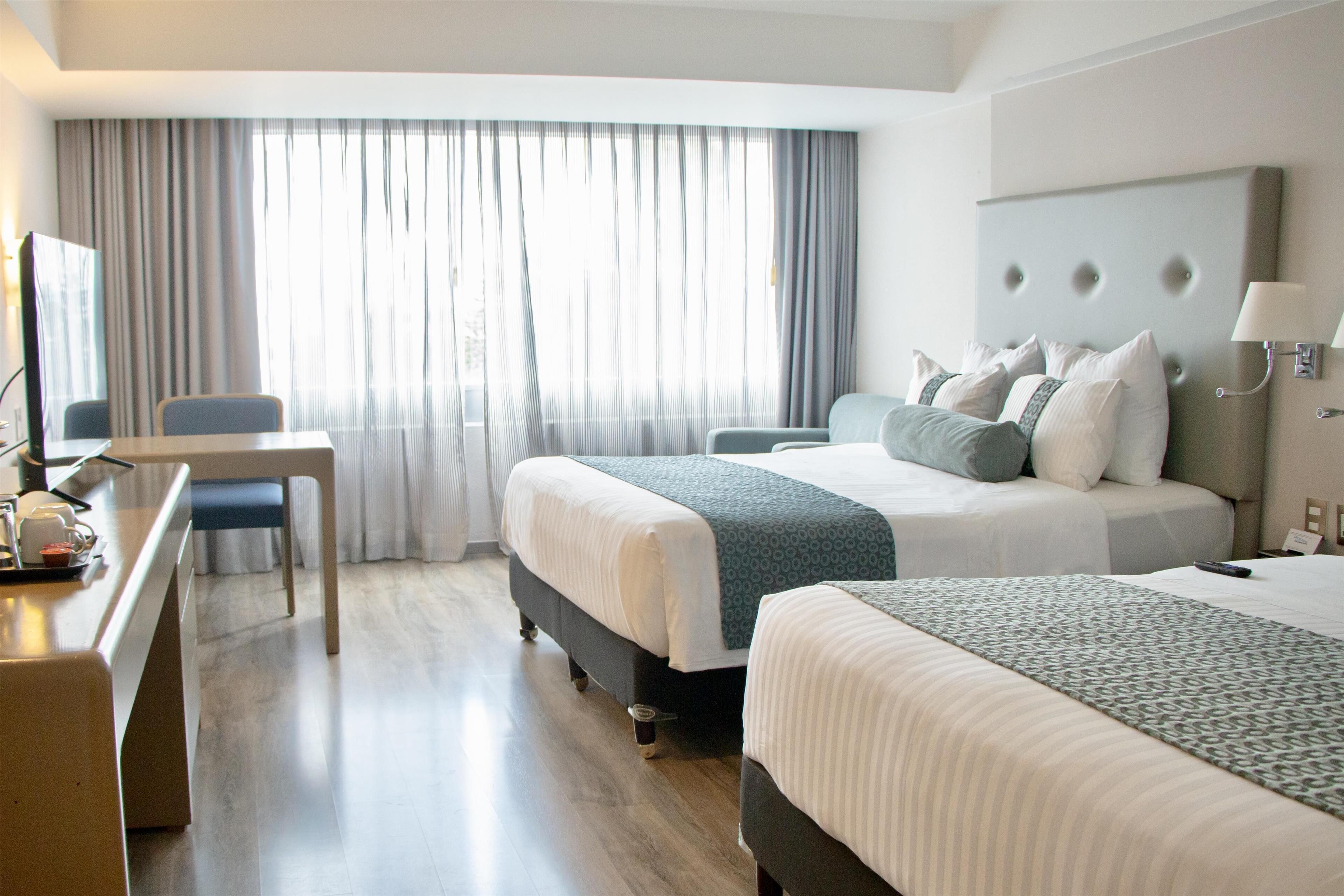 A hotel room with two beds, a desk, and a TV.