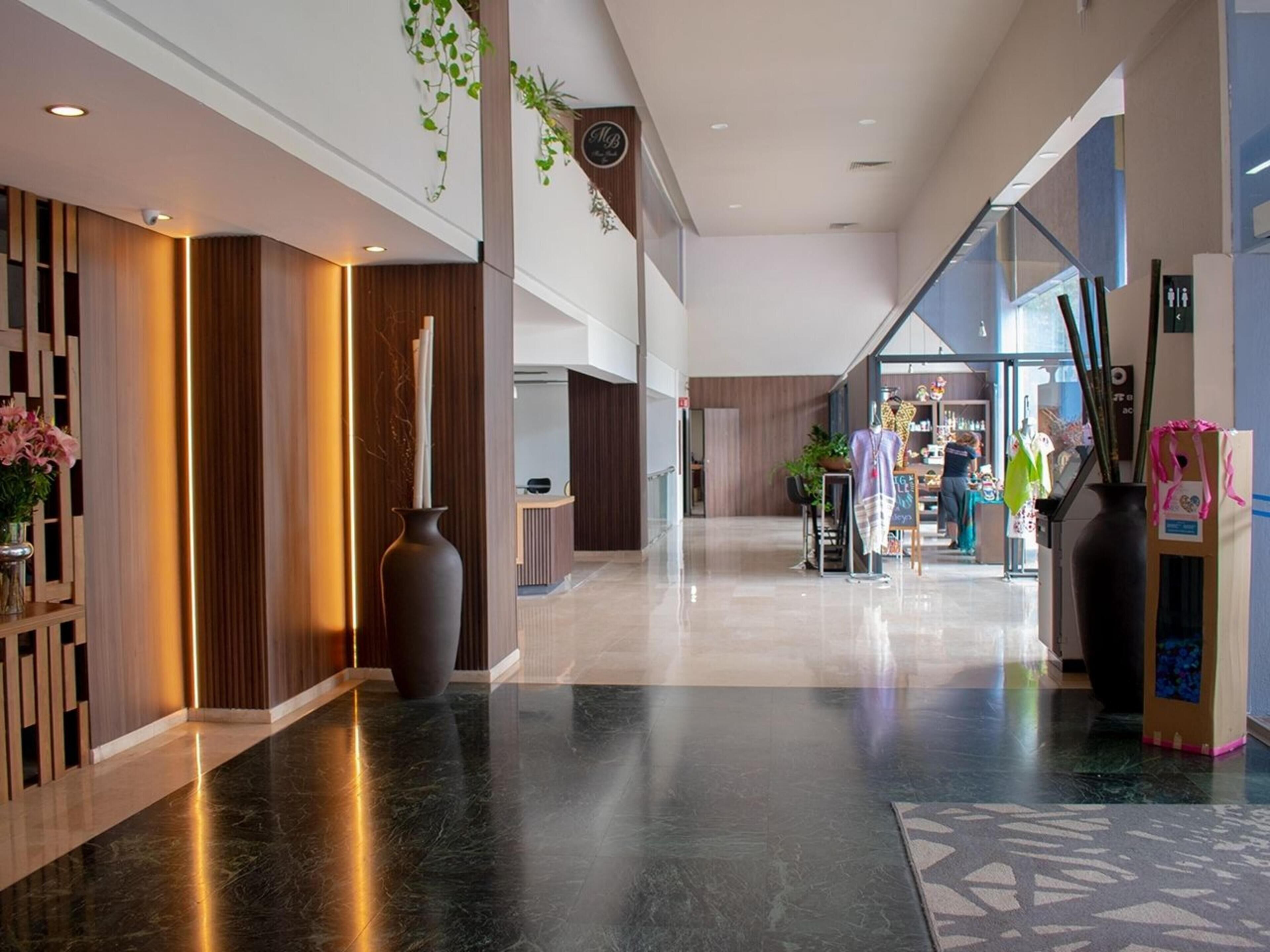 A modern hotel lobby with a reception desk, a large vase, and a patterned carpet.
