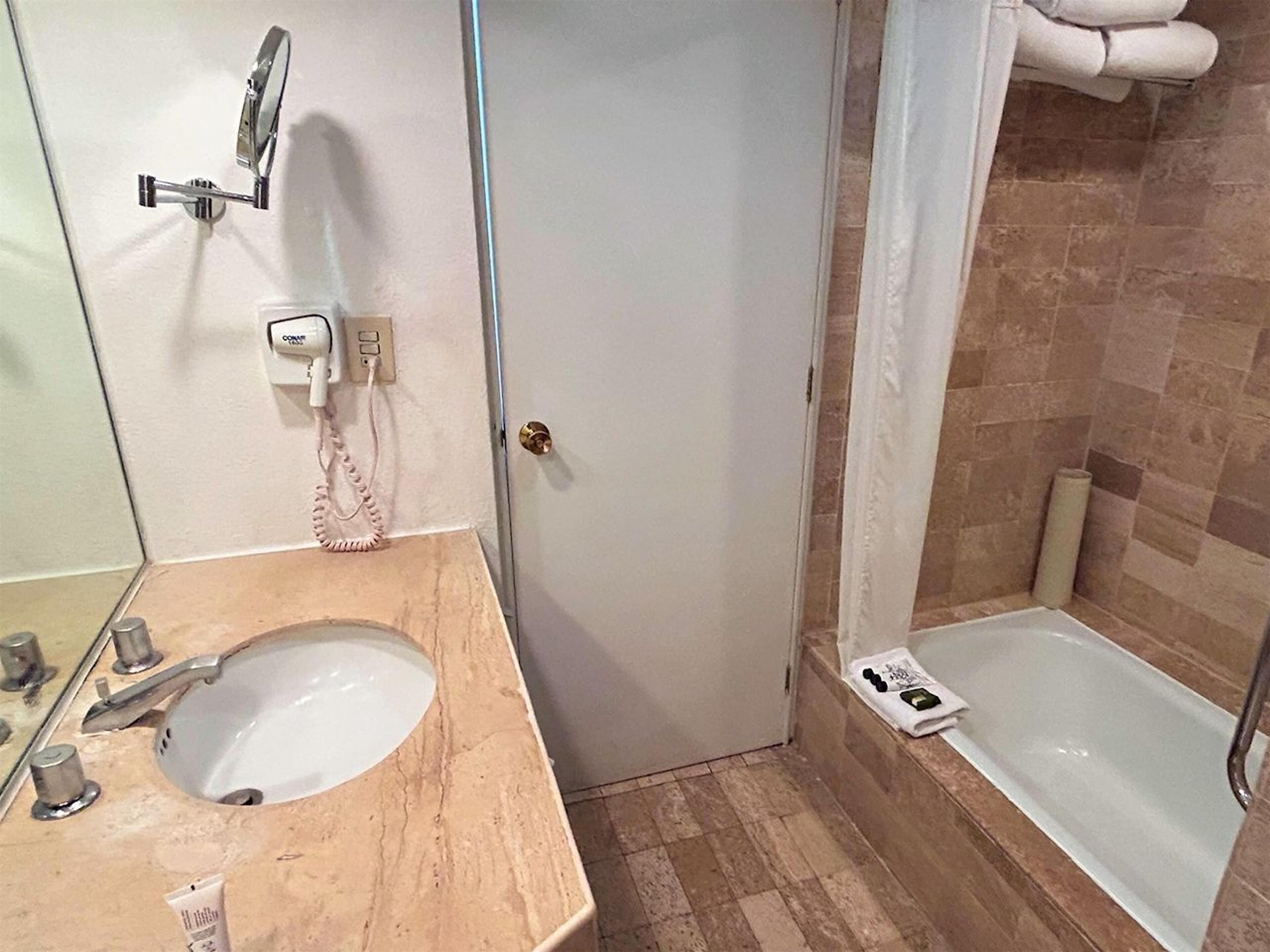 A bathroom with a sink, mirror, towel rack, and a shower area.
