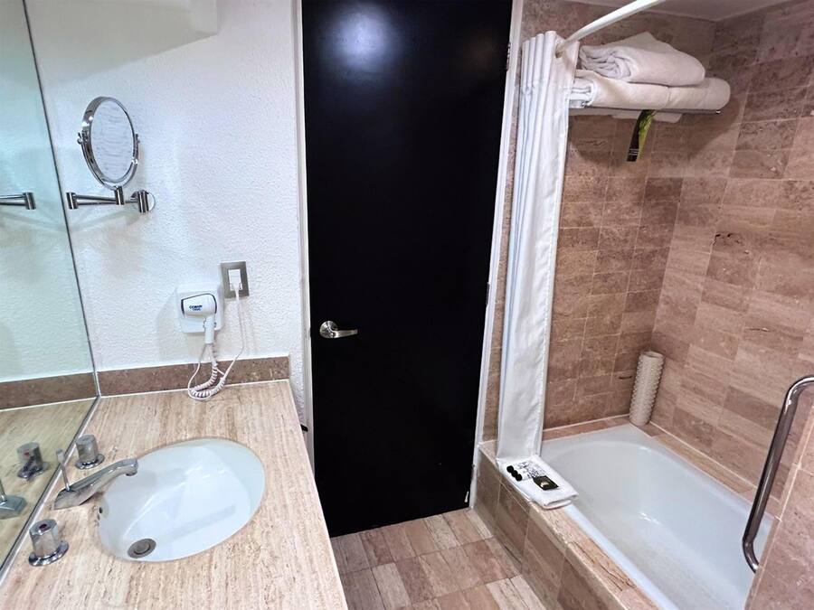 Un baño con un lavamanos blanco, un espejo, una puerta negra y una zona de ducha con perchero.