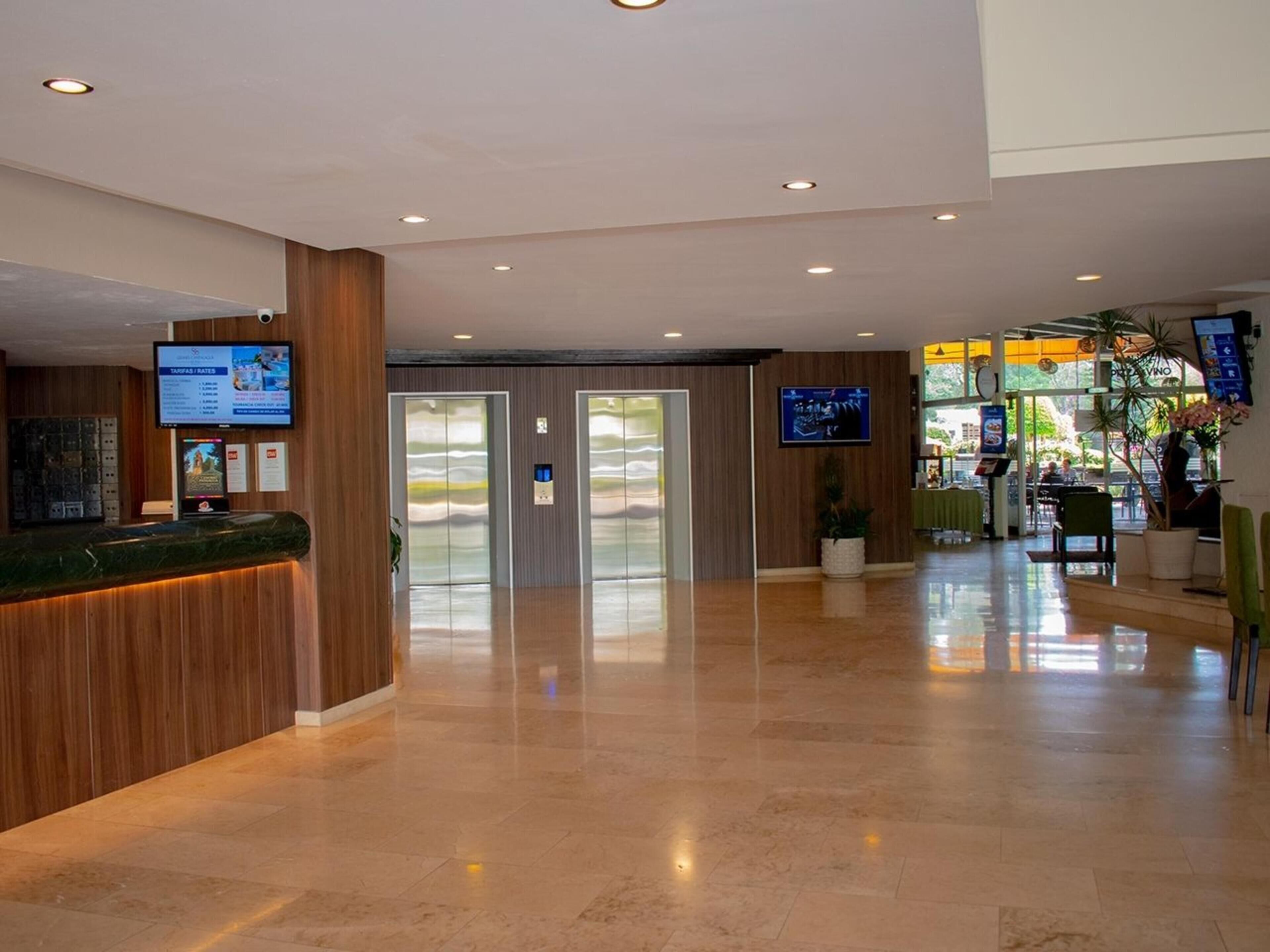 A hotel lobby with a reception desk, elevators, and a dining area.