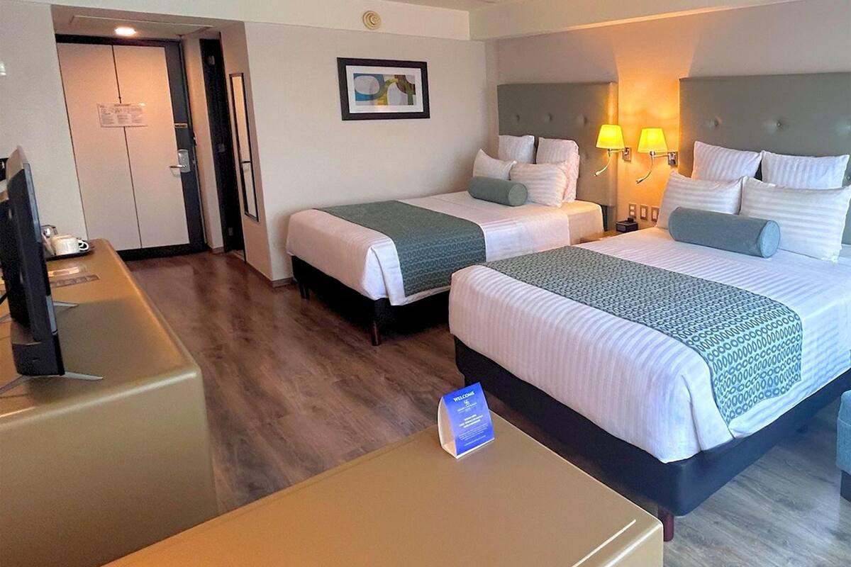 A hotel room with two beds, a desk, a chair, a TV, and a door.
