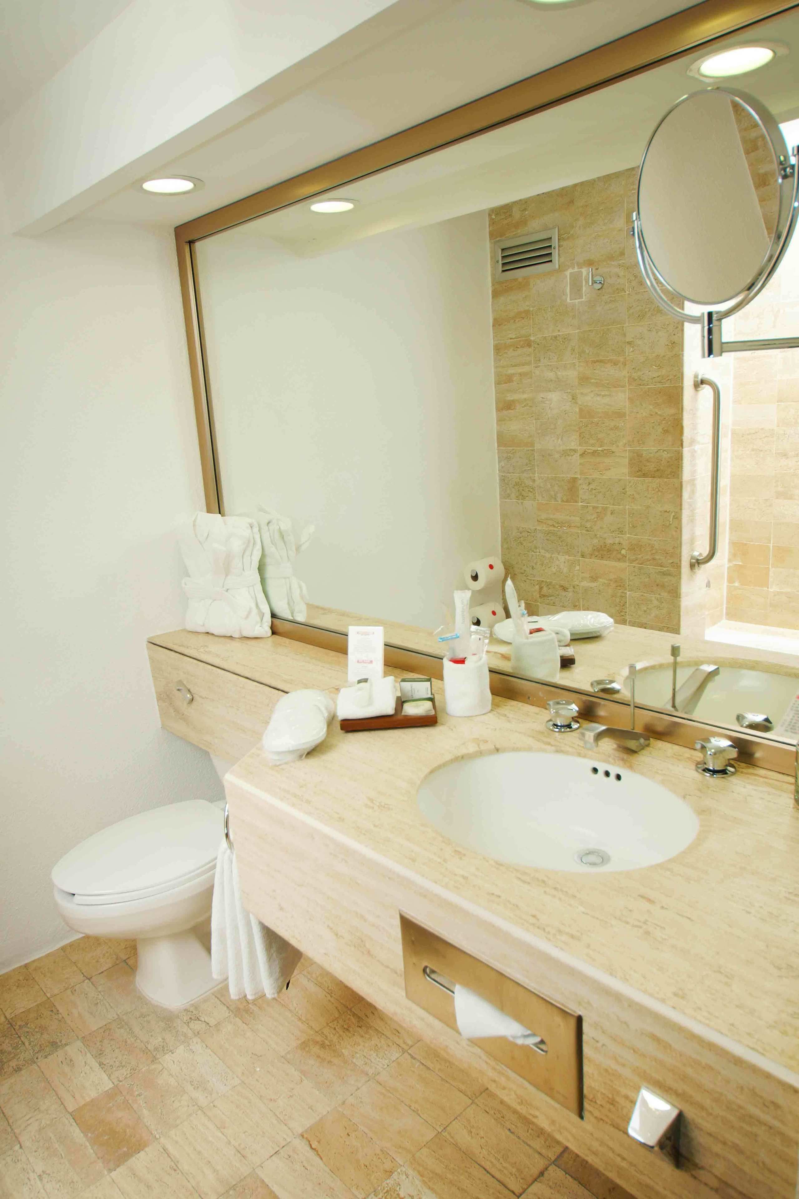 A modern bathroom with a beige countertop, a large mirror, a white sink, and a toilet.