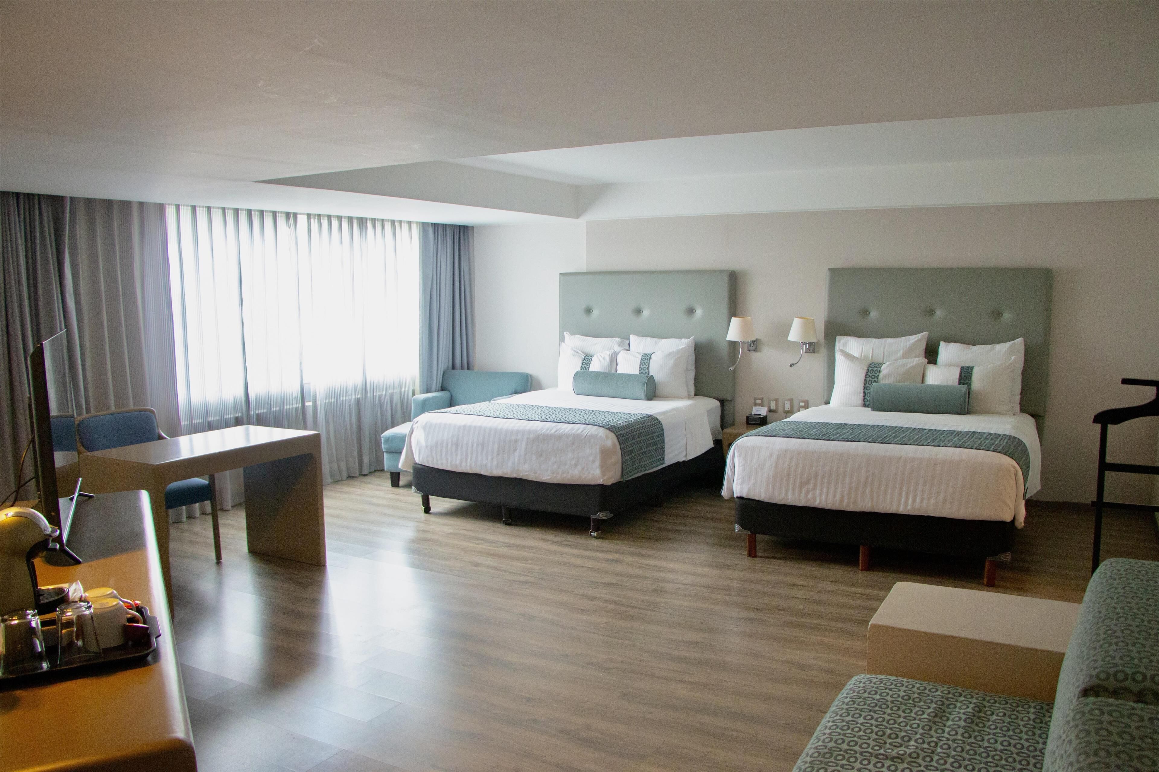 A hotel room with two beds, a desk, and a chair.