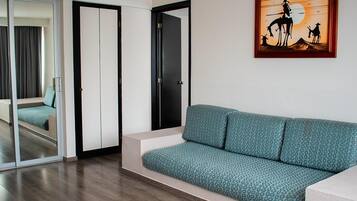 A modern living room with a teal patterned sofa, a sliding glass door leading to a balcony, and a framed artwork depicting a cowboy scene.