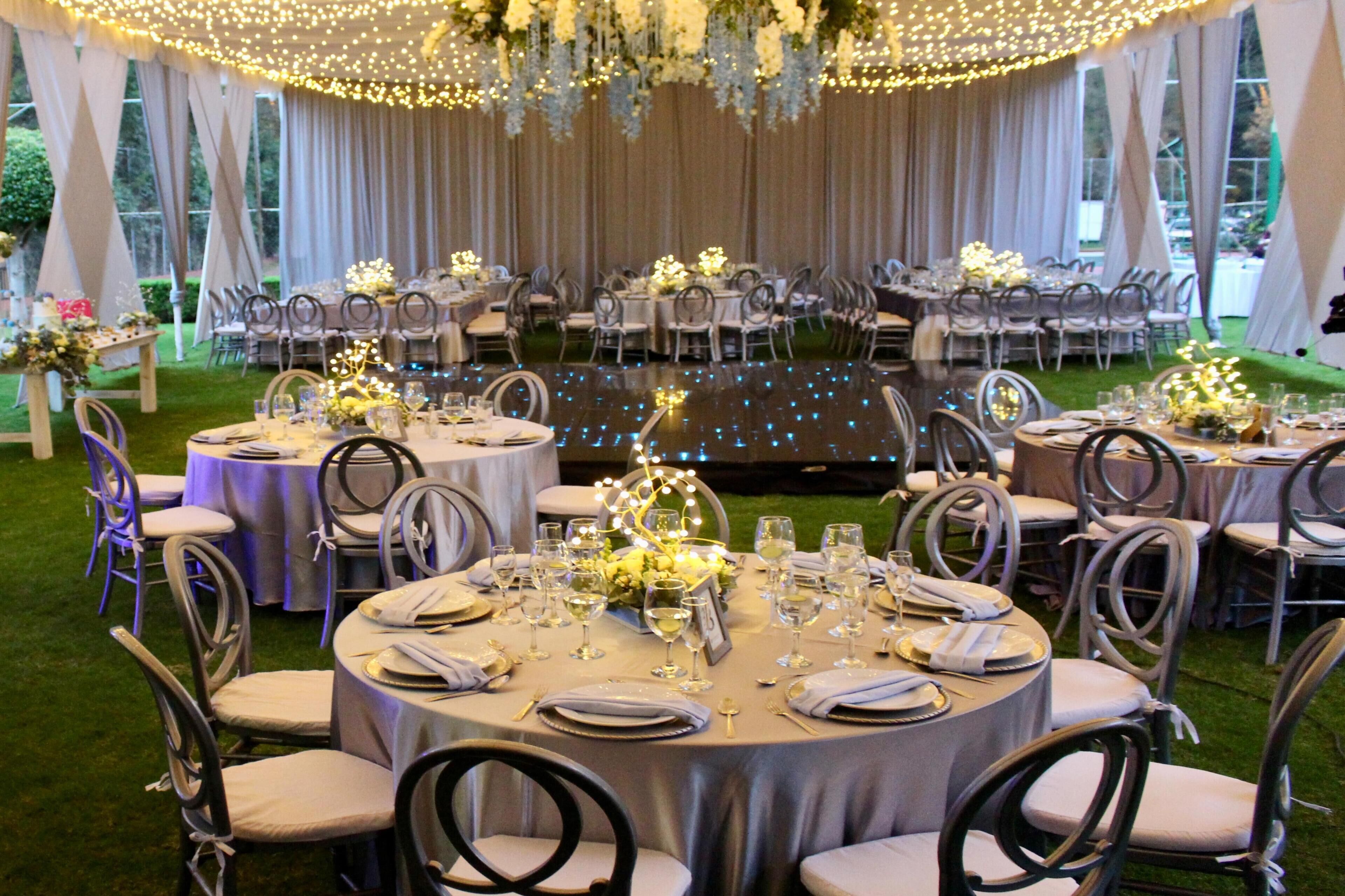 A banquet hall with round tables set for a formal event, featuring chairs, table settings, and decorative lighting.