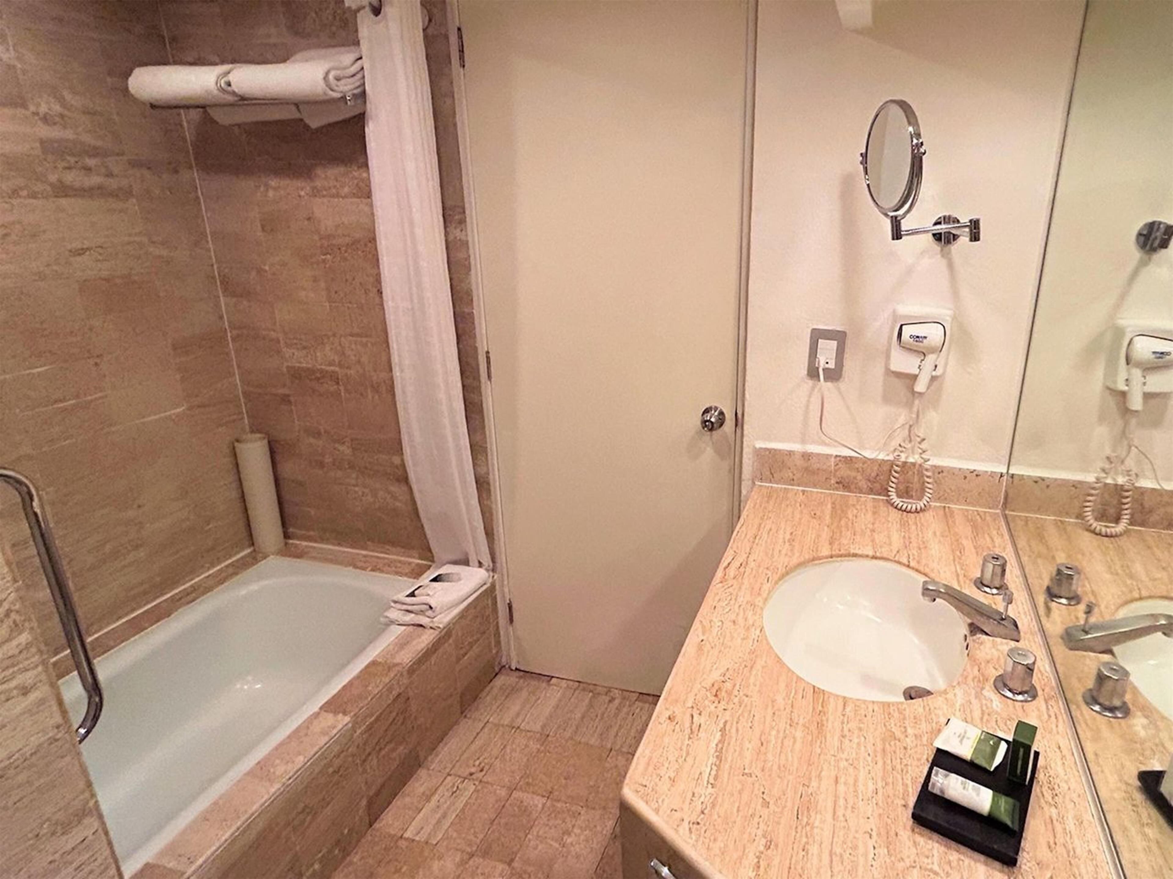 A bathroom with a bathtub, a sink, a mirror, and a towel rack.