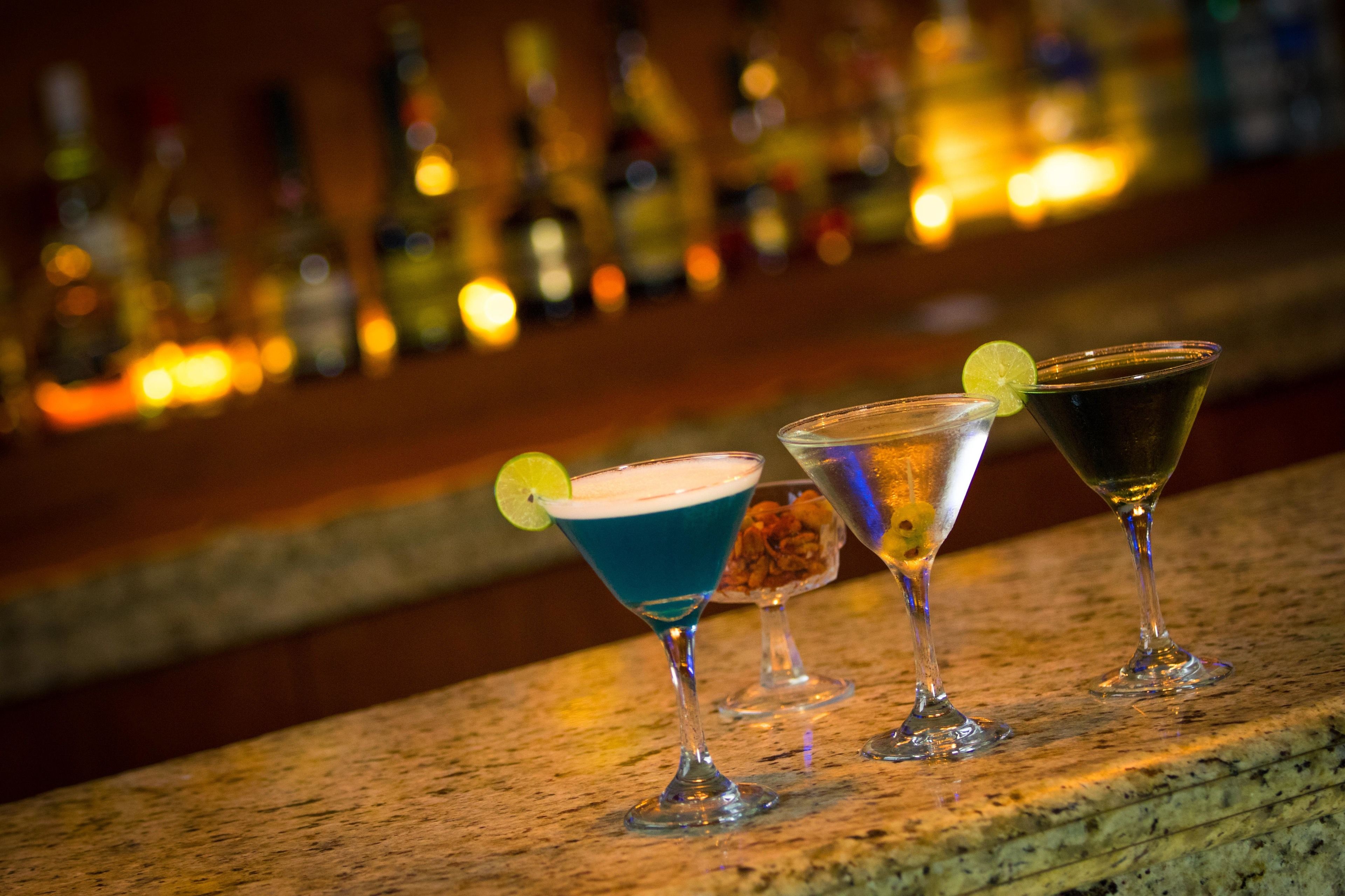 Tres vasos de martini sobre una barra con un fondo desenfocado de botellas.