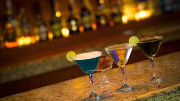 Three martini glasses on a bar counter with a blurred background of bottles.