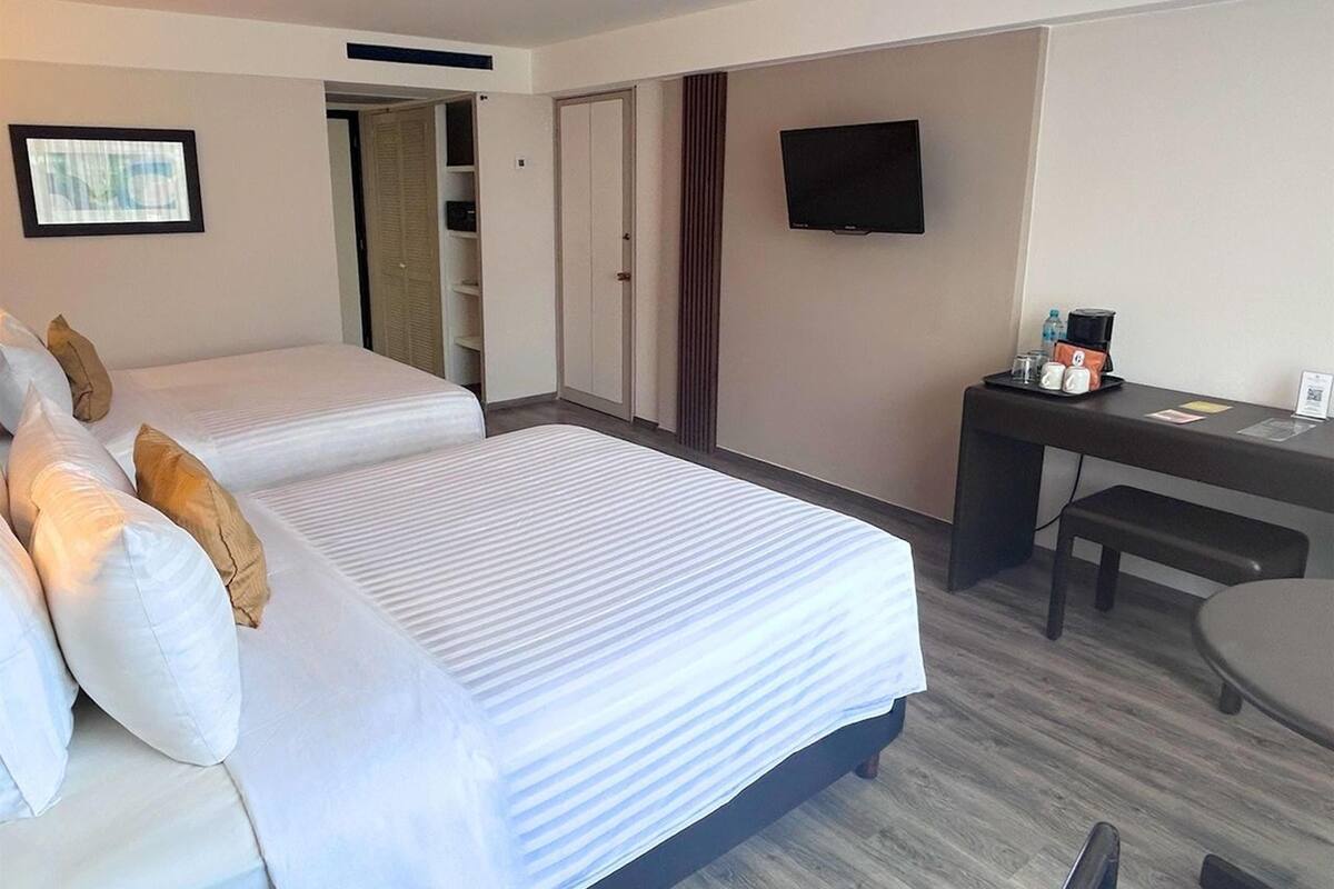 A hotel room with two beds, a desk, a television, and a coffee maker.