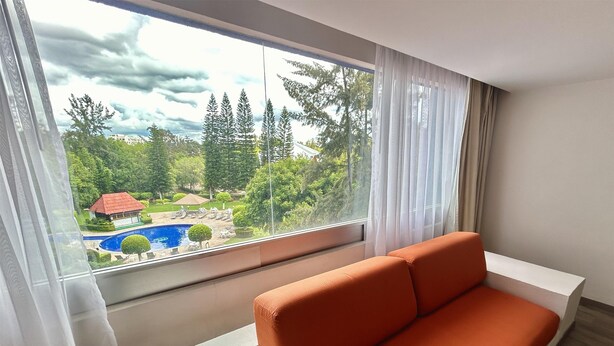 A modern room with a large window, a white sofa, and a view of a pool and greenery. - Grand Cantalagua Hotel Morelia, BW Signature Collection (Morelia)