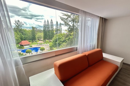 A modern room with a large window, a white sofa, and a view of a pool and greenery.
