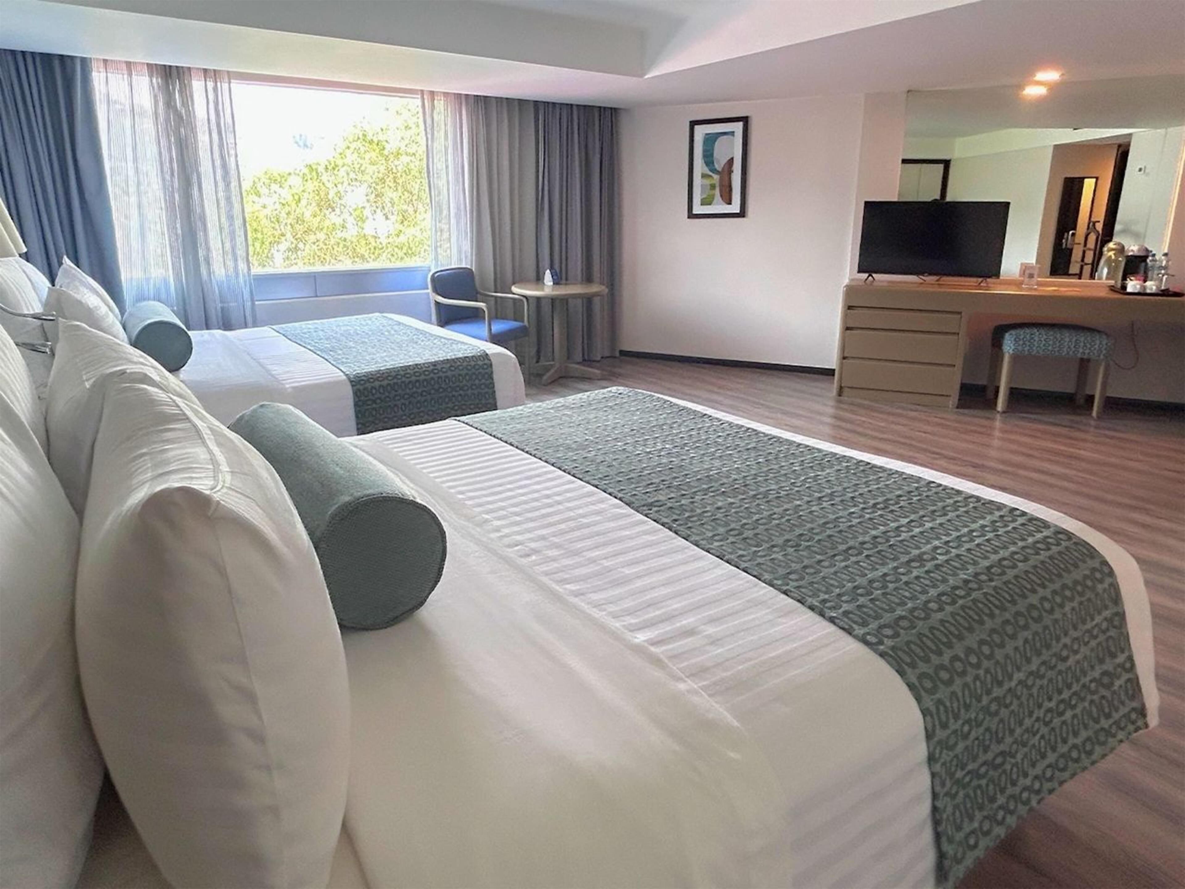 Une chambre d’hôtel avec deux lits, un bureau, une chaise, une télévision et une fenêtre avec des rideaux.