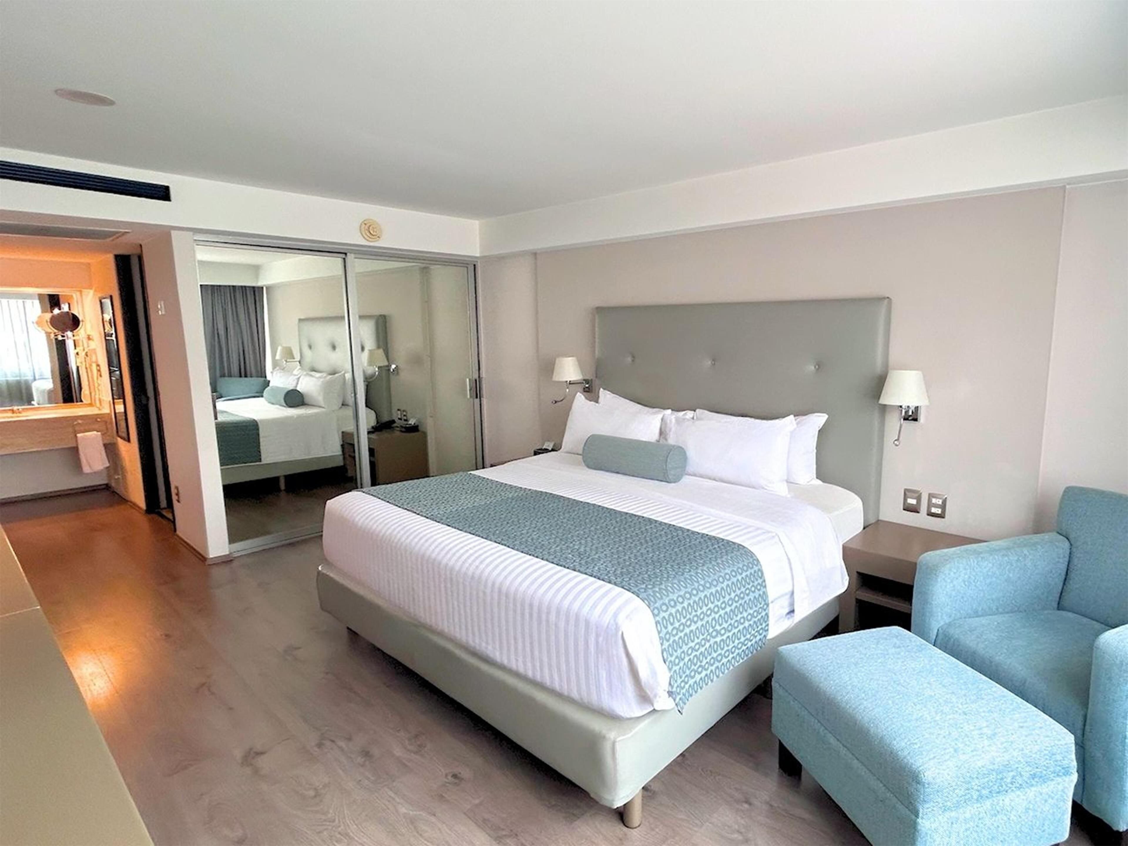 A modern hotel room with a large bed, a seating area, and a mirror.