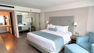 A modern hotel room with a large bed, a seating area, and a mirror.
