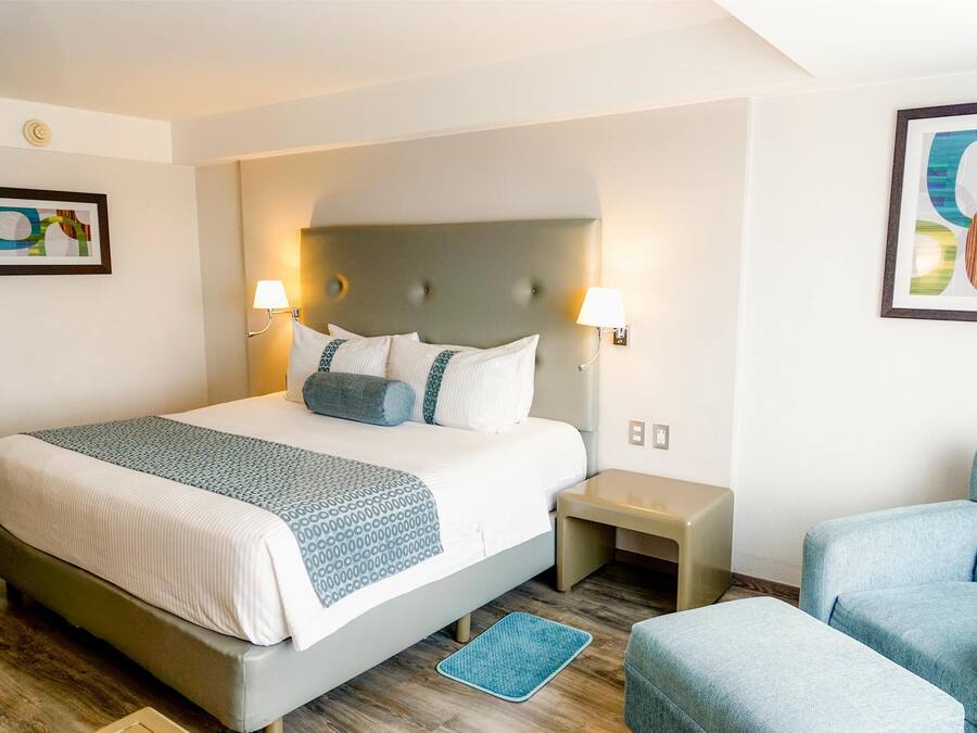 A hotel room with a large bed, two bedside tables, a chair, and artwork on the walls.