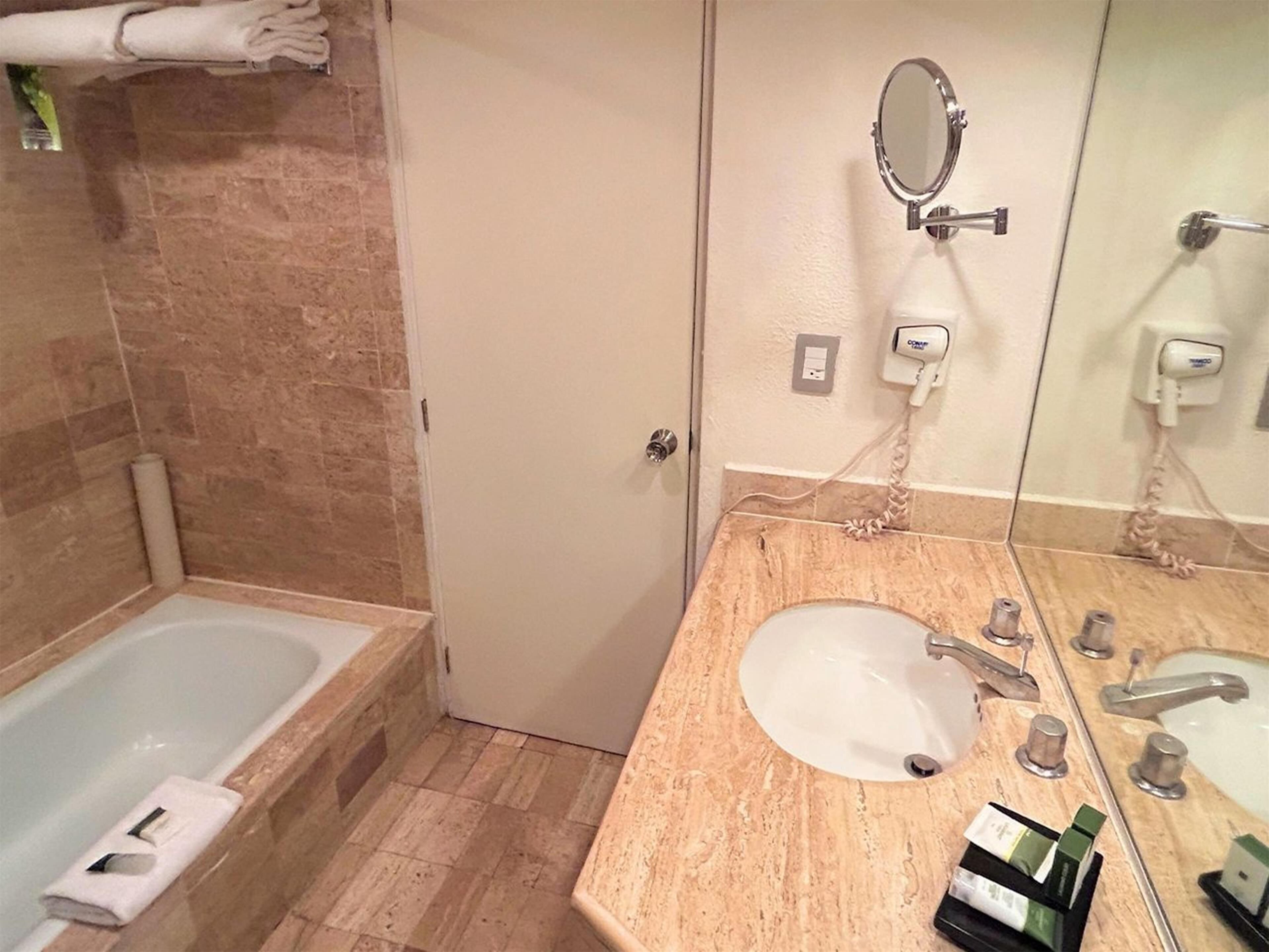 A bathroom with a bathtub, a sink, a mirror, and toiletries.