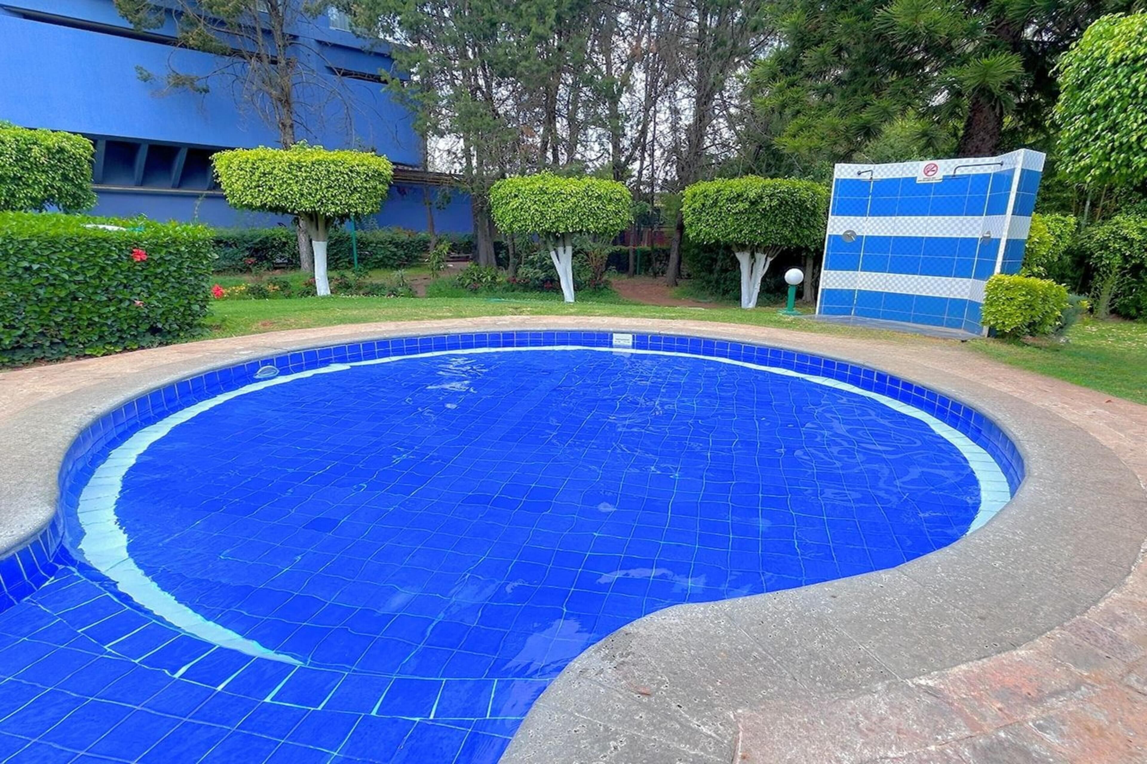 Una piscina circular con azulejos azules, rodeada por un borde de hormigón, y un edificio con fachada azul al fondo.