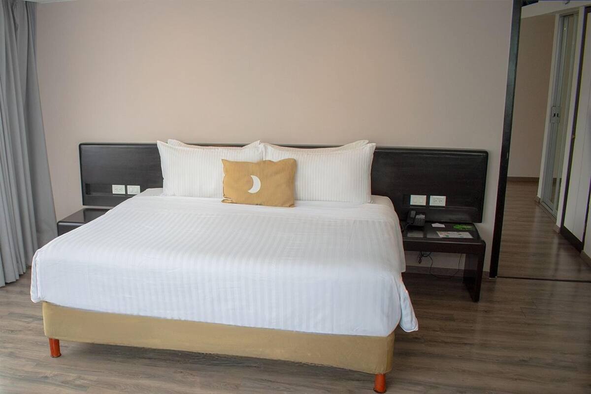 A hotel room with a large bed, two bedside tables, a nightstand, and a door leading to another room.