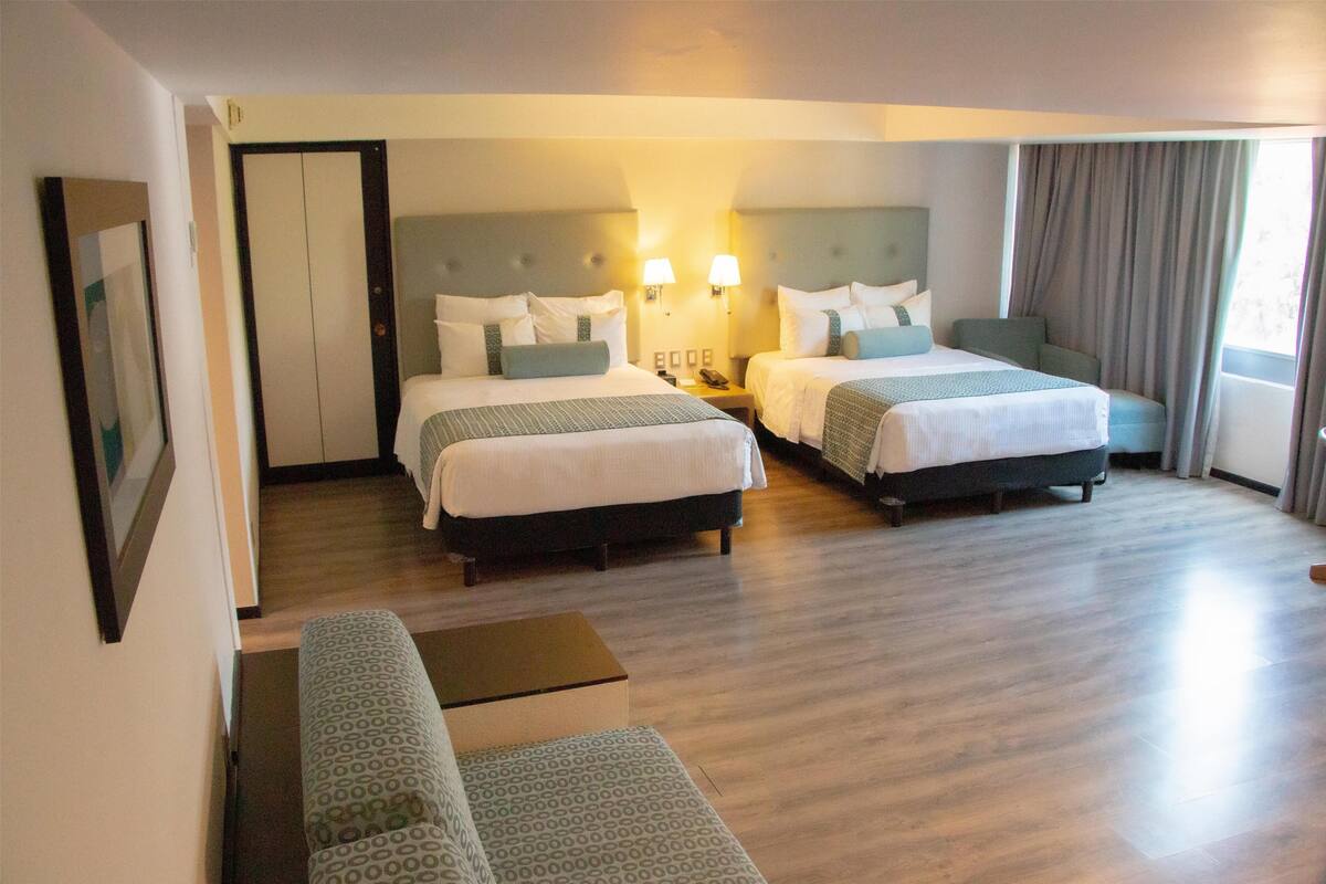 A hotel room with two beds, a sofa, and a small table.