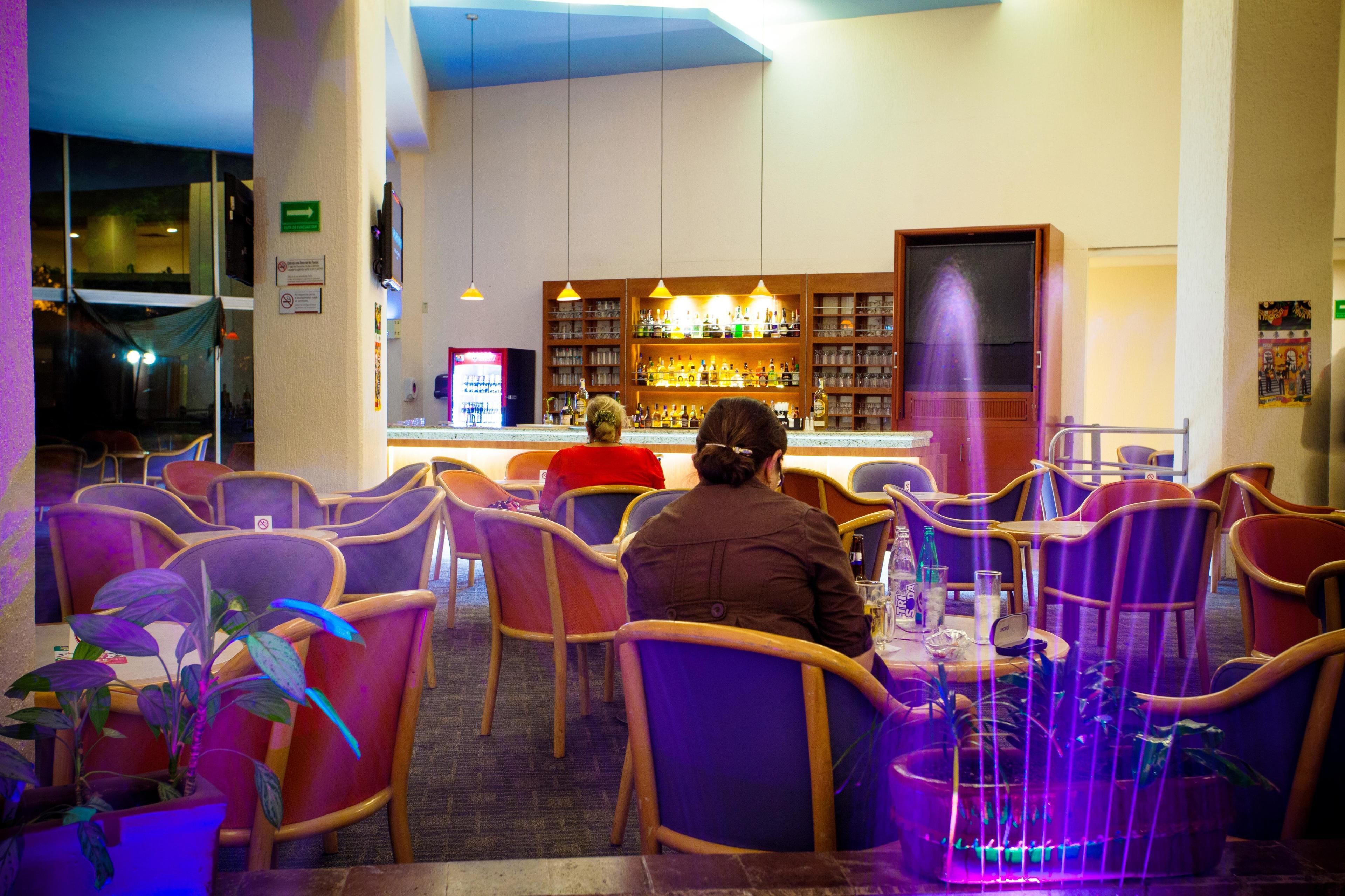 A restaurant with purple chairs, a bar area, and a view of the street outside.