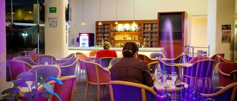 Un restaurante con sillas moradas, una zona de bar y vistas a la calle.