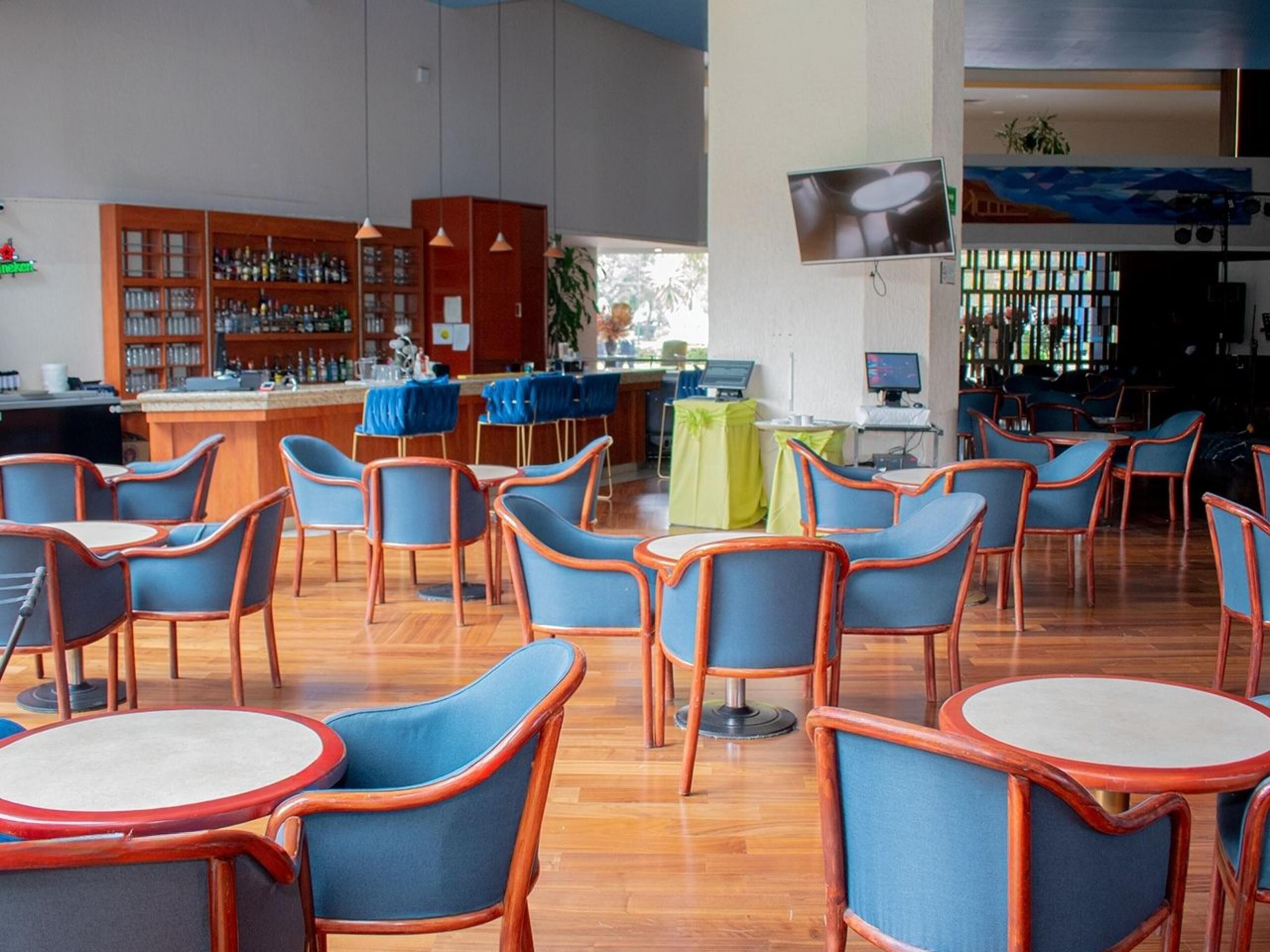 Un vestíbulo de hotel con zona de bar, diferentes disposiciones de asientos y una pantalla de televisión.