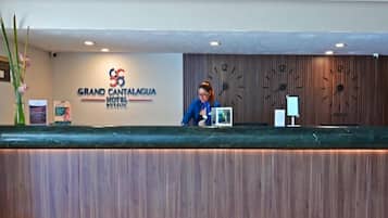 Mostrador de recepción en el Hotel Grand Cantagua, con un panel de pared de madera, un reloj y una pantalla digital.