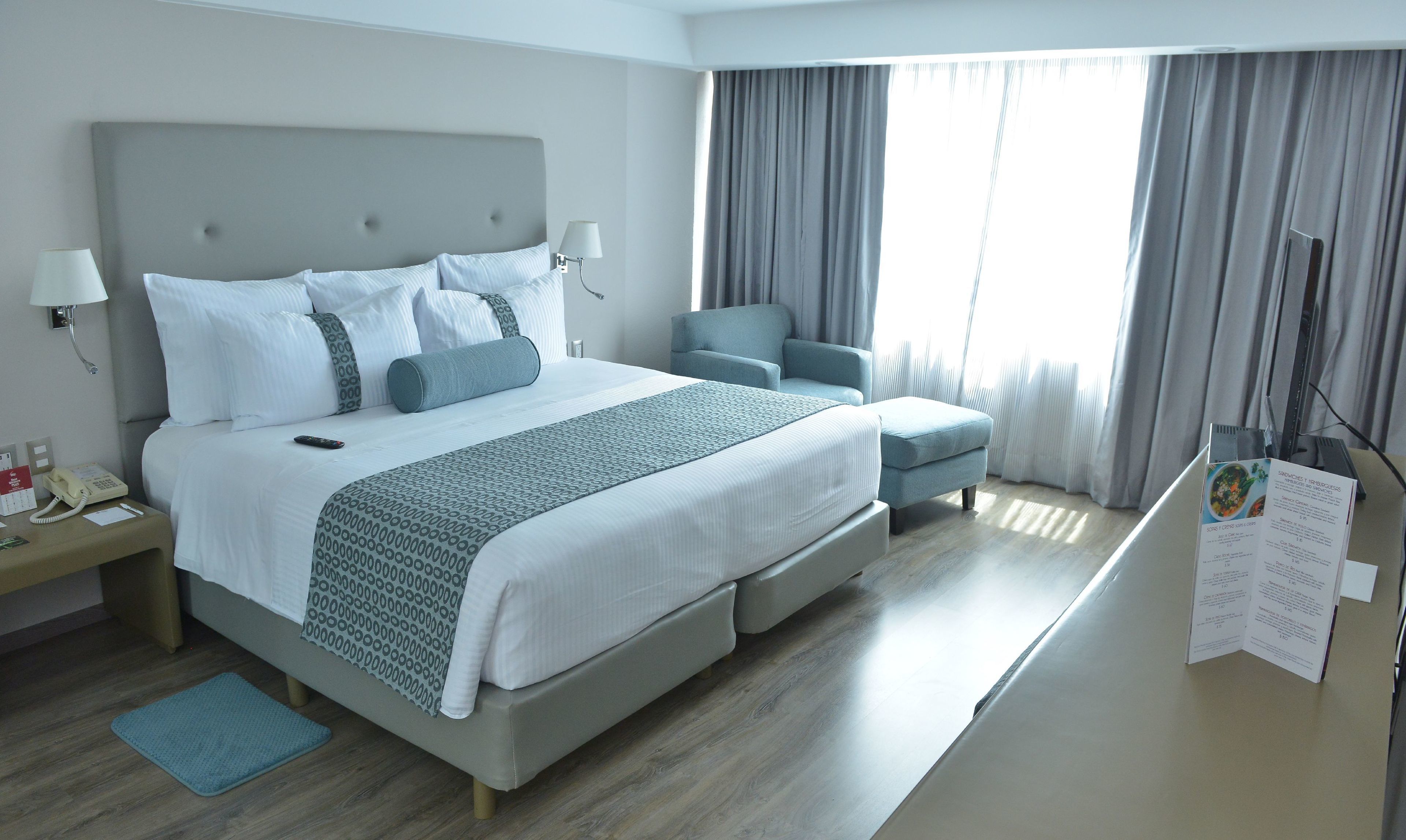 A hotel room with a large bed, a desk with a phone, a chair, and a menu stand.