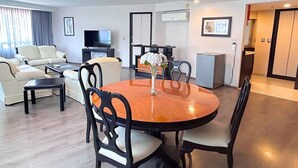 A modern living room with a round wooden dining table, black chairs, a sofa set, a flat-screen TV, and a small kitchen area. - Grand Cantalagua Hotel Morelia, BW Signature Collection (Morelia)