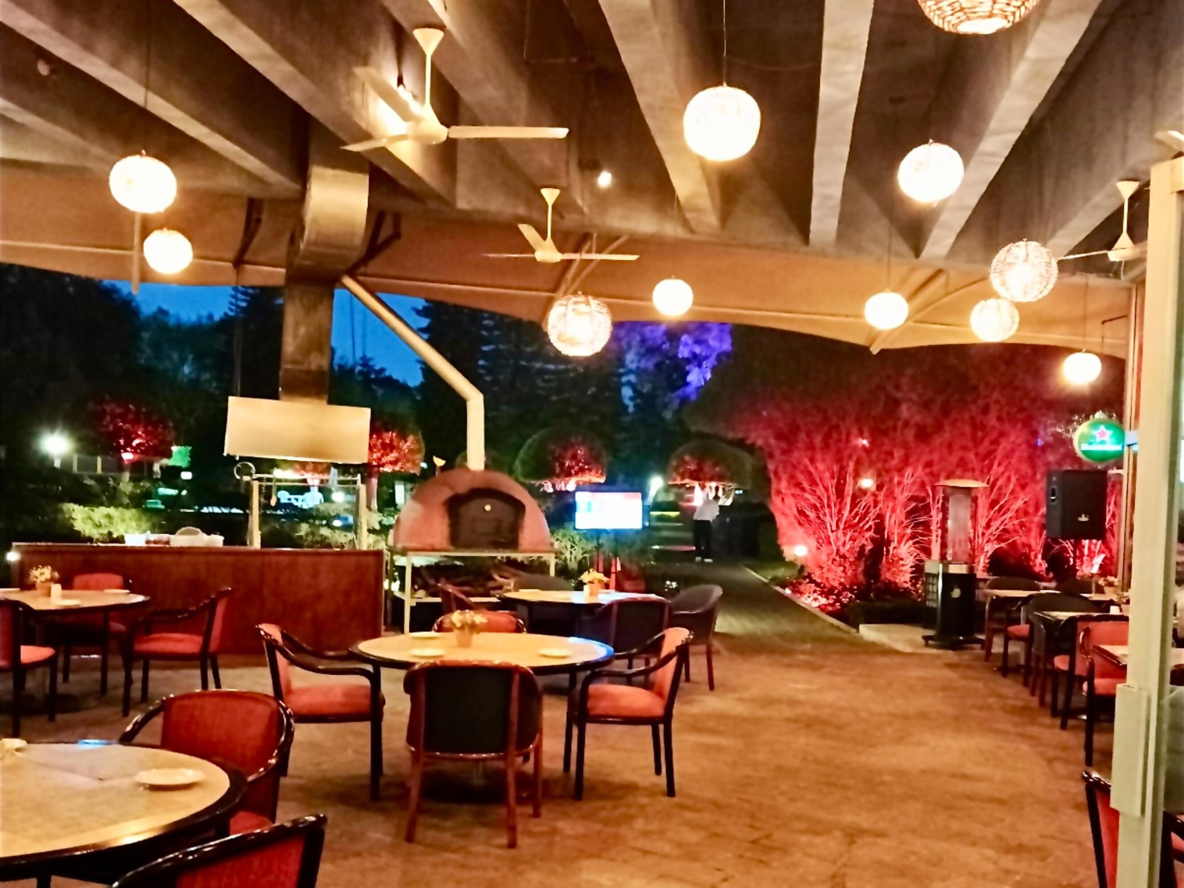 An outdoor dining area with round tables and chairs, a central grill, and ceiling fans.