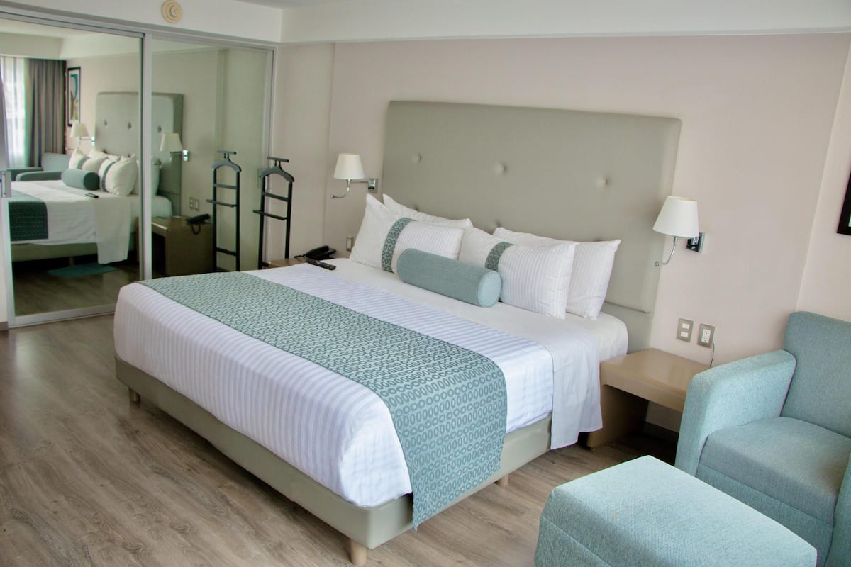 A hotel room with a large bed, a nightstand, a chair, a mirror, and a wardrobe.