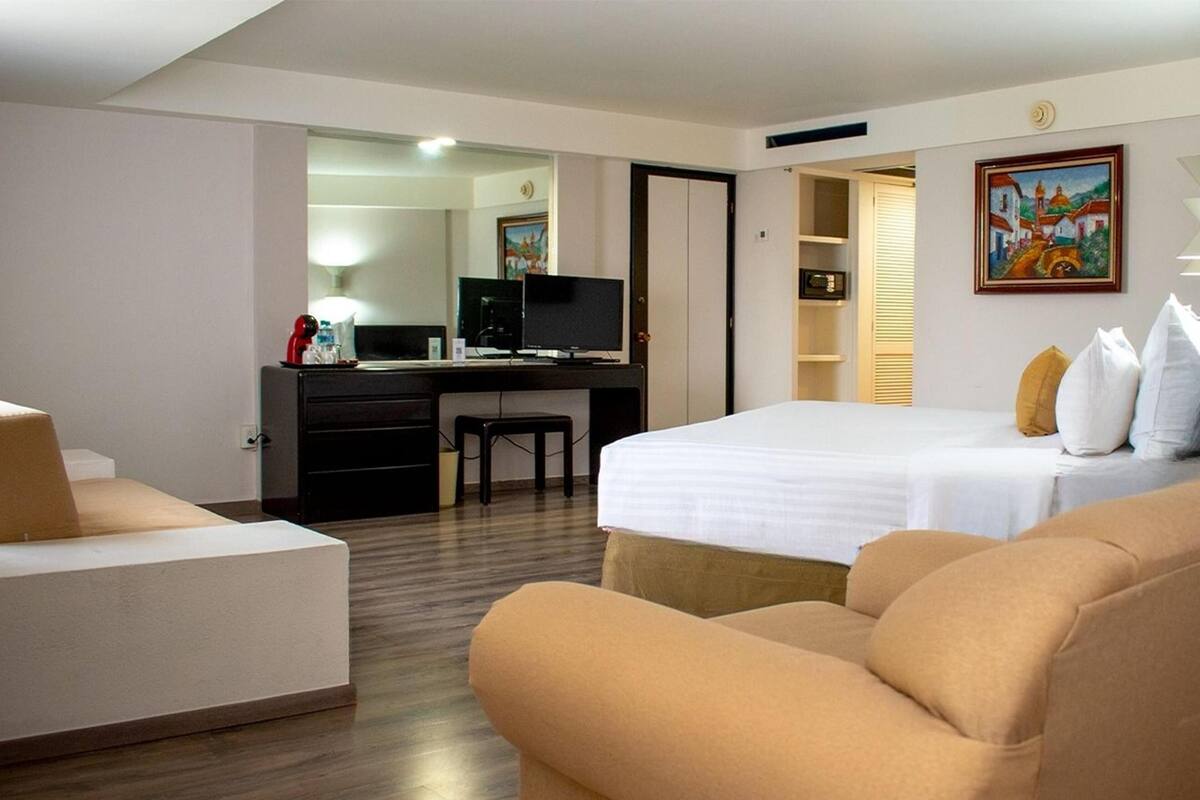 A hotel room with a bed, a desk with a computer, a chair, and a sofa.