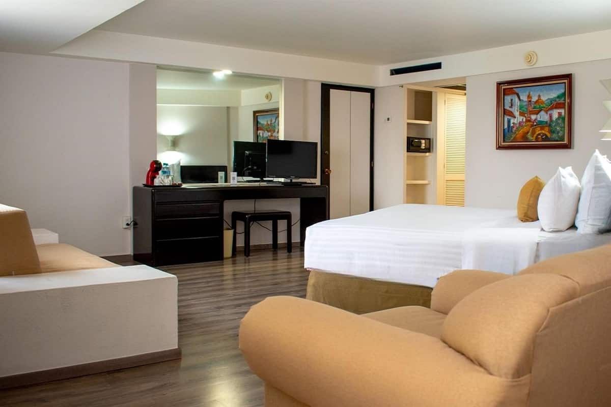Ett hotellrum med en säng, ett skrivbord med en dator, en stol och en soffa.