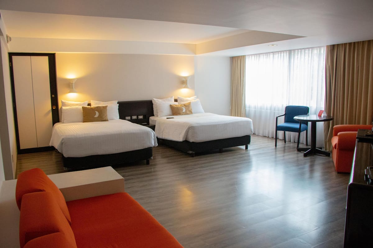 A hotel room with two beds, a desk, a chair, and a sofa.
