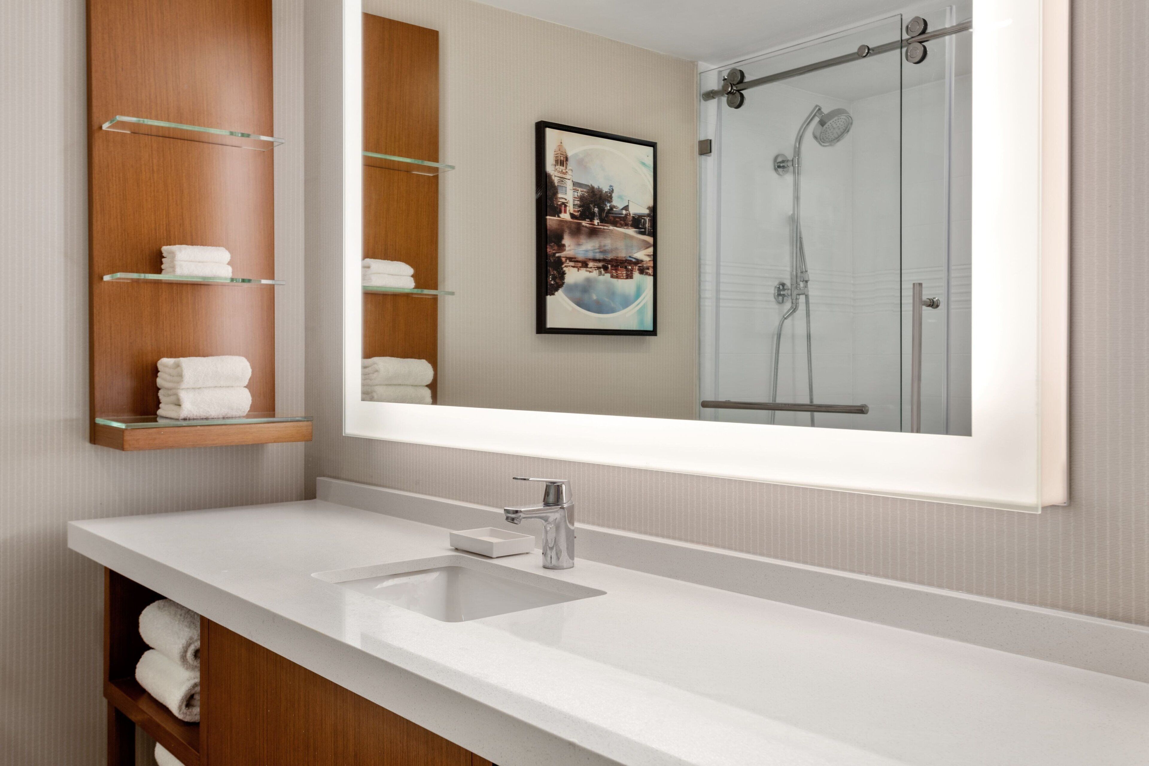 A modern bathroom with a large mirror, a white sink, and a glass-enclosed shower.