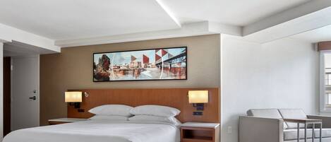 Une chambre d’hôtel avec un grand lit, deux tables de chevet avec des lampes, un canapé et un tableau représentant un paysage urbain accroché au mur.