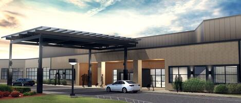 A modern building with a covered entrance, a parking area, and a landscaped garden.