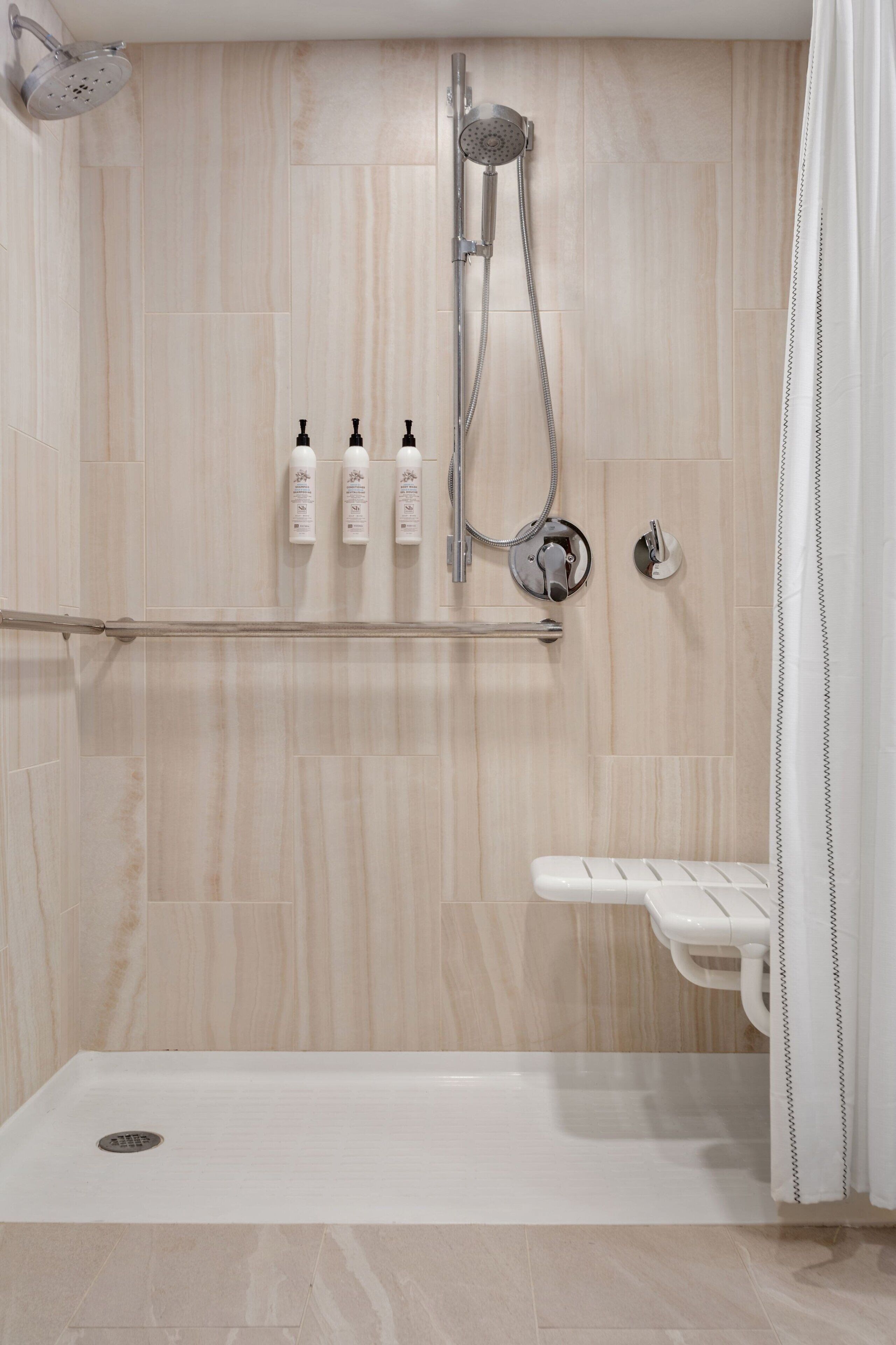 Un espacio de ducha moderno con un cabezal de ducha manual, un grifo empotrado en la pared y tres botellas de champú sobre una repisa.
