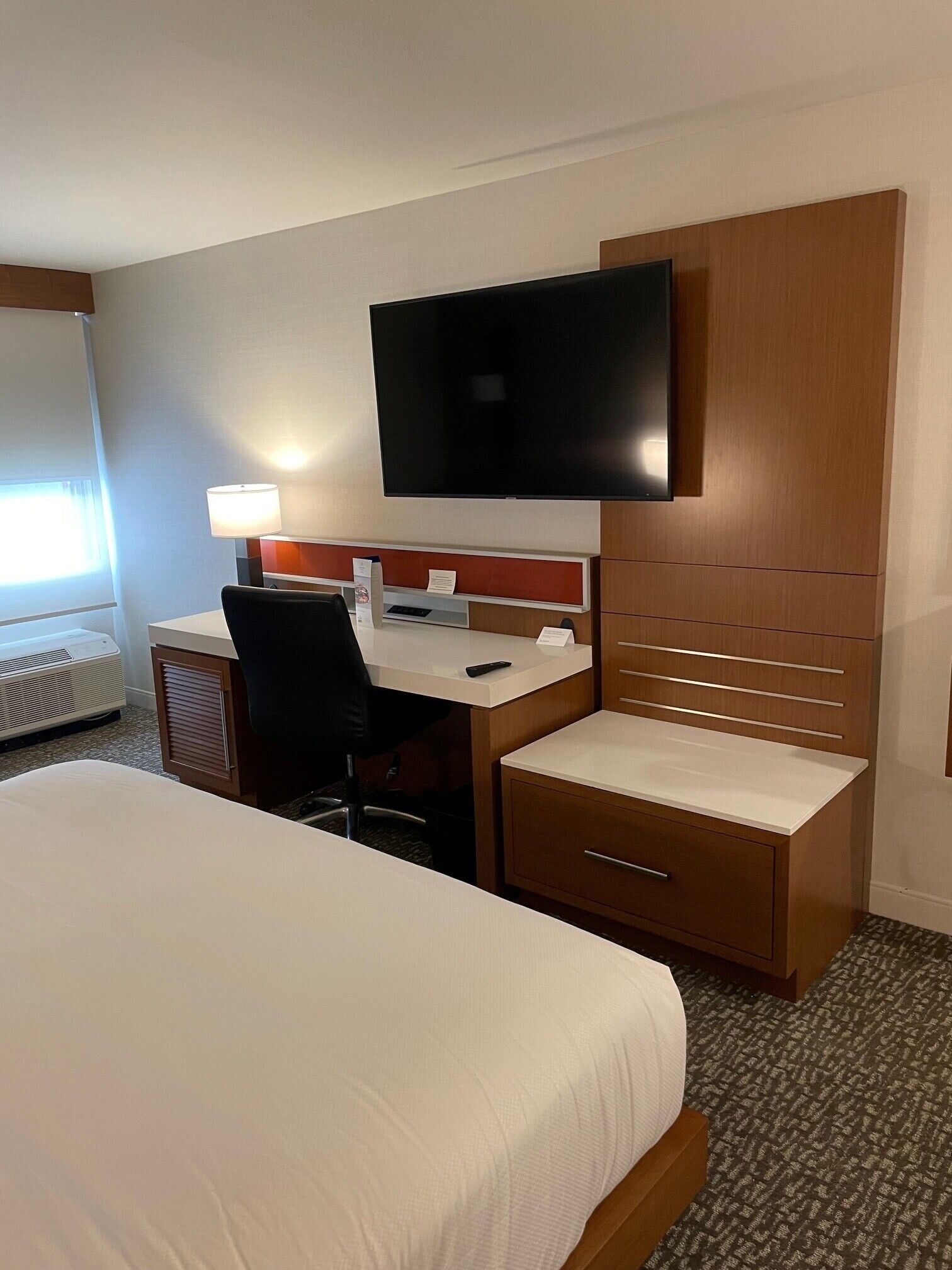 Une chambre d’hôtel comprenant un lit, un bureau avec une chaise, un téléviseur fixé au mur et un petit placard.