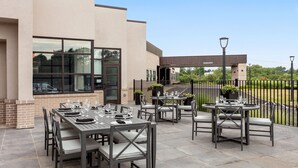 Terrassa exterior amb diverses taules i cadires, una paret de maó i un edifici al fons.